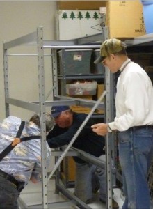Steve Grissom, Gary Davis, and Larry Foltz setting up shelving units in storage room.