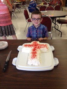 Dylan Brzozowski is shown guarding the special cake made by Peggy Spitzenberger for the reception honoring new members joining the church on August 23.